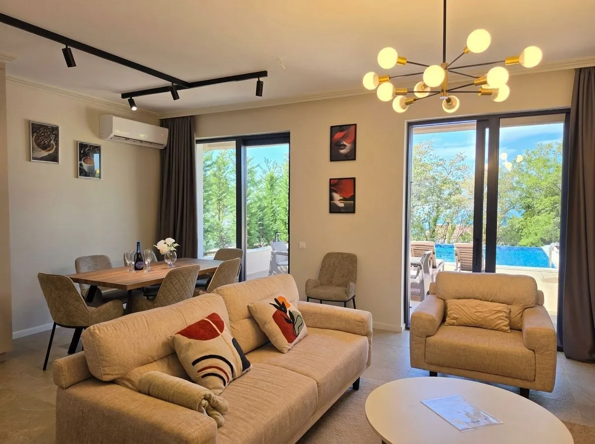 Spacious living room with a sofa set, dining area, and access to the terrace with a swimming pool.