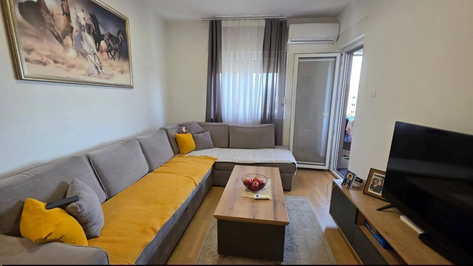 Dnevna soba sa ugaonom garniturom, stočićem i televizorom.
