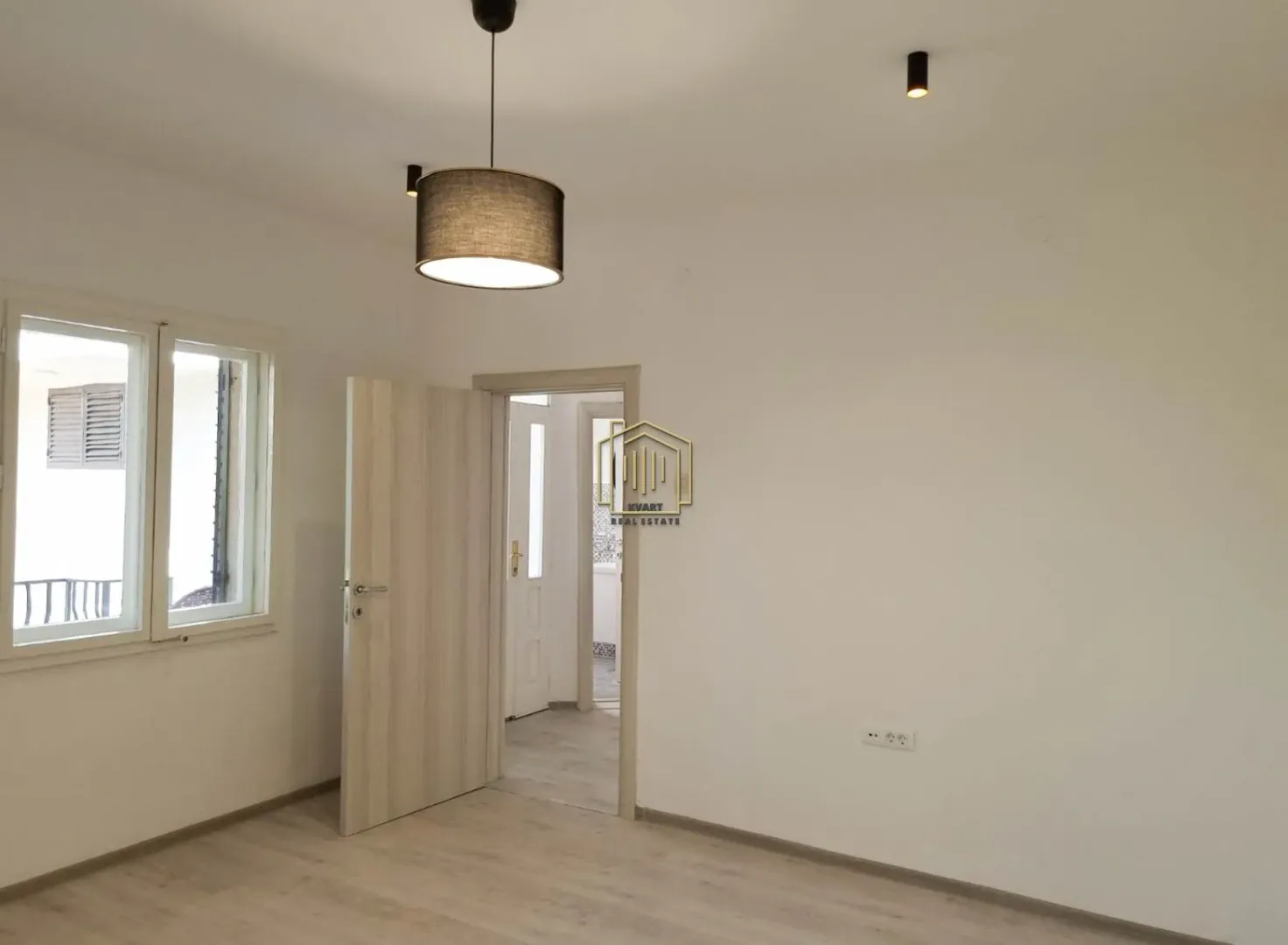 Empty room with light laminate flooring, a pendant light, and an open door leading to the hallway.