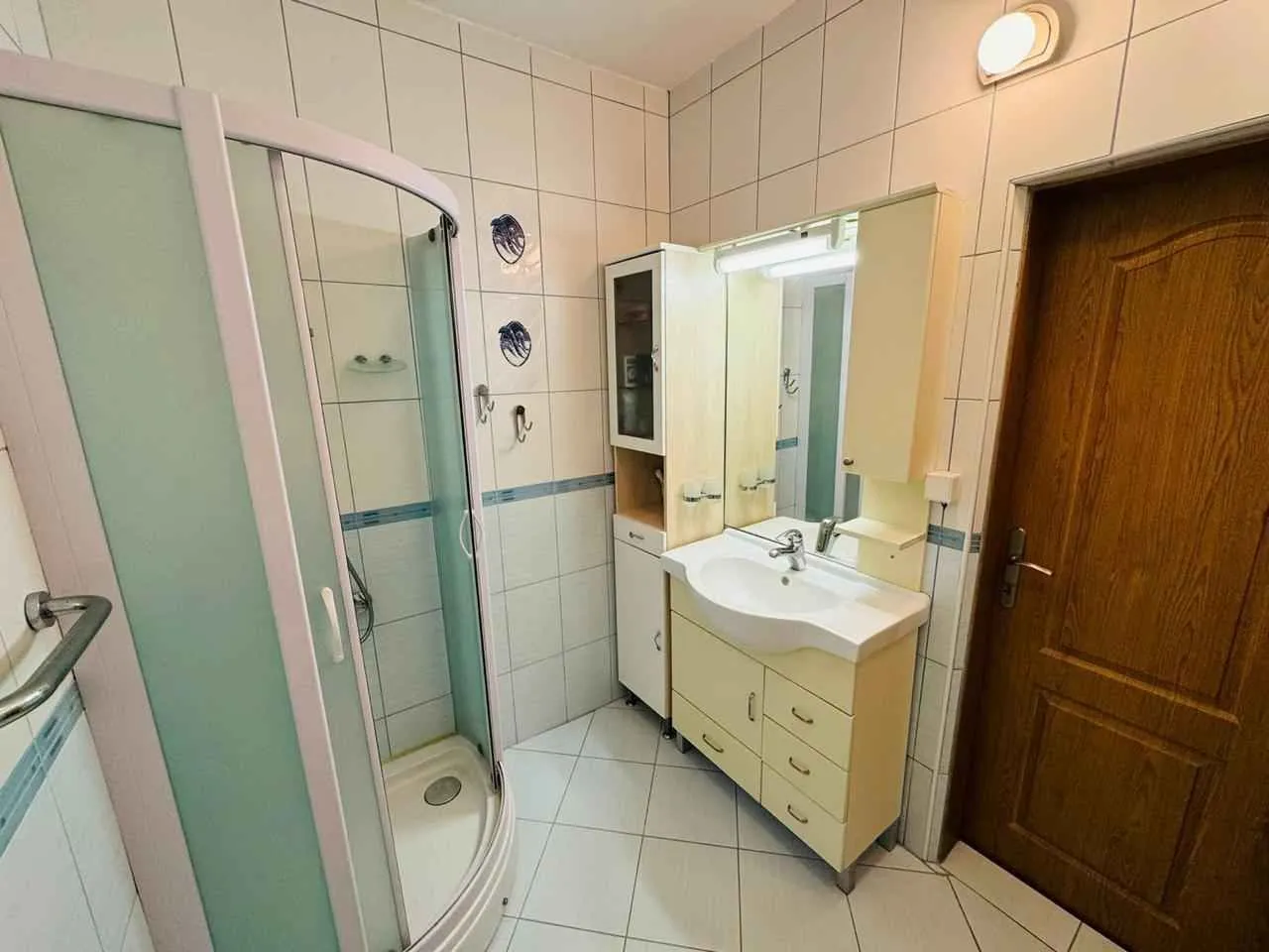 Kupatilo opremljeno tuš kabinom, umivaonikom sa ormarićem i ogledalom.