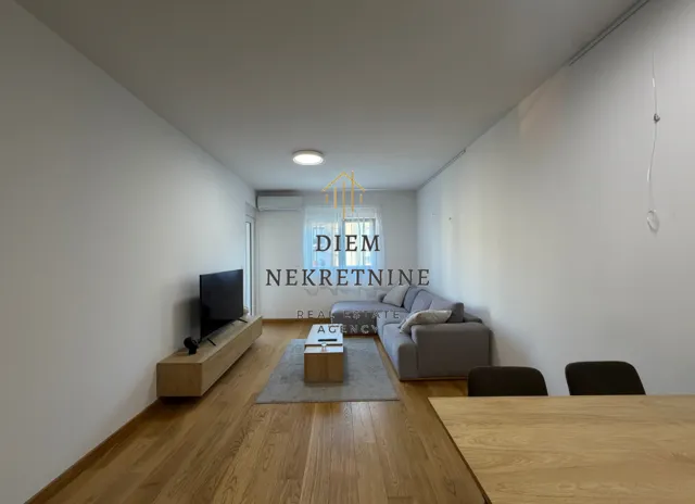 Dnevna soba sa garniturom za sjedenje, TV komodom i trpezarijskim stolom u prvom planu.