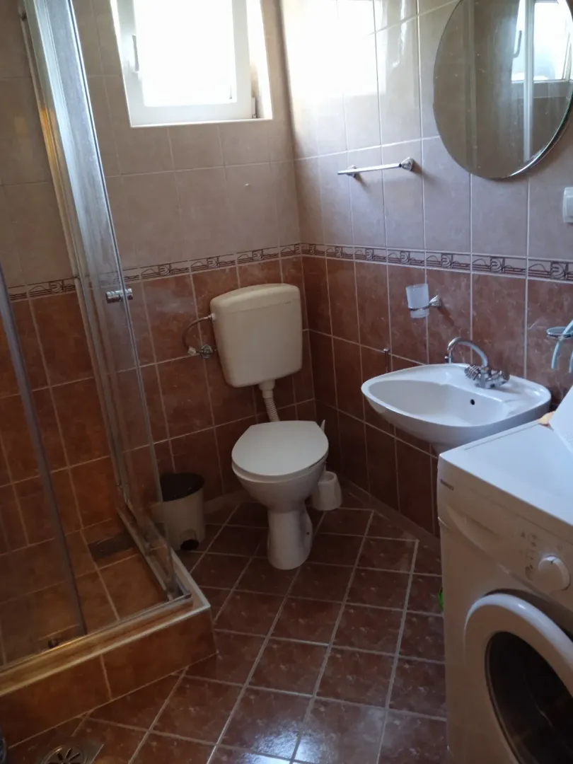 Smaller bathroom with a shower cabin, sink, toilet, and washing machine.