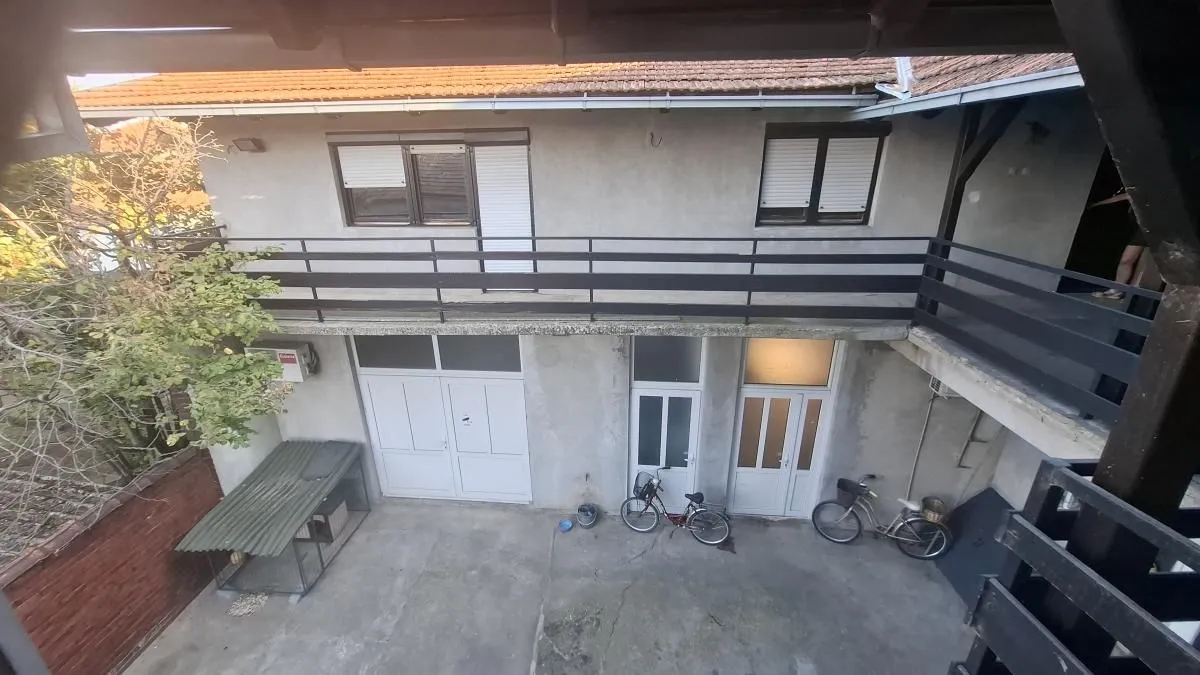 Pogled sa sprata na dvorište i fasadu kuće sa balkonom.
