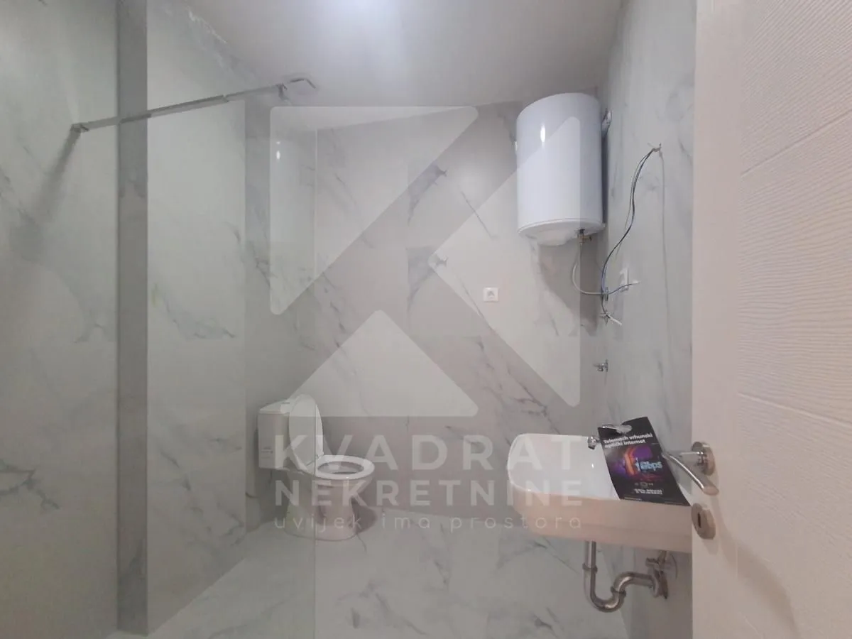 Small bathroom tiled with marble-look tiles featuring a walk-in shower, toilet, and washbasin.