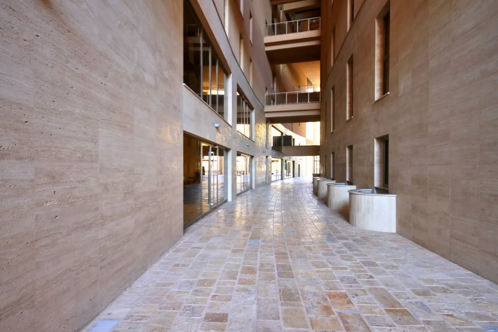 Paved walkway between modern buildings with stone facades.