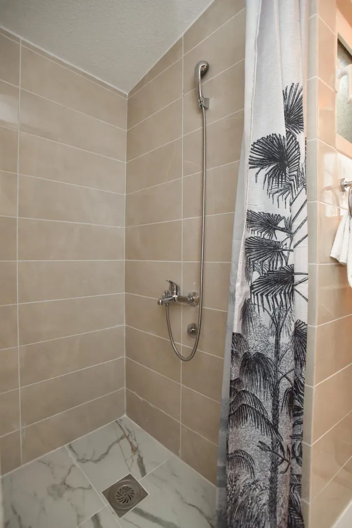 Shower enclosure with beige tiles and a curtain with palm tree motifs.
