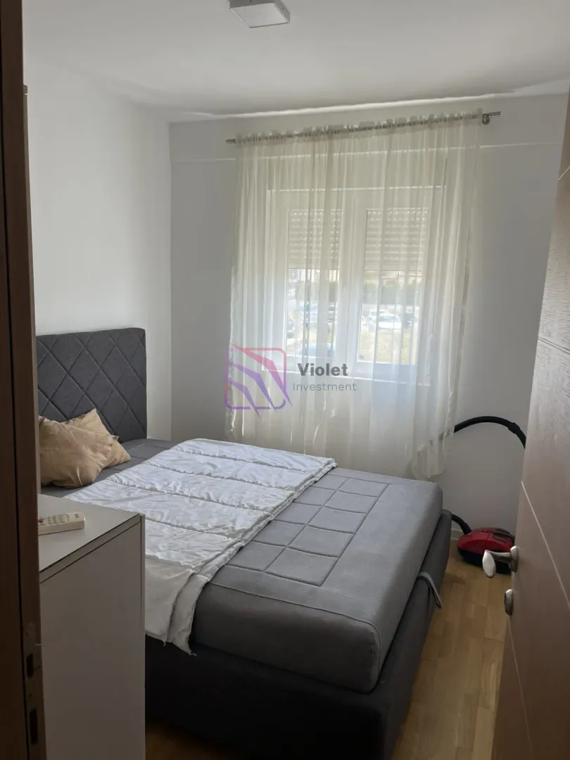 Spavaća soba sa bračnim krevetom i prozorom sa bijelim zavjesama.
