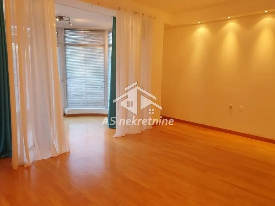 Empty living room with wooden flooring and large windows with curtains.