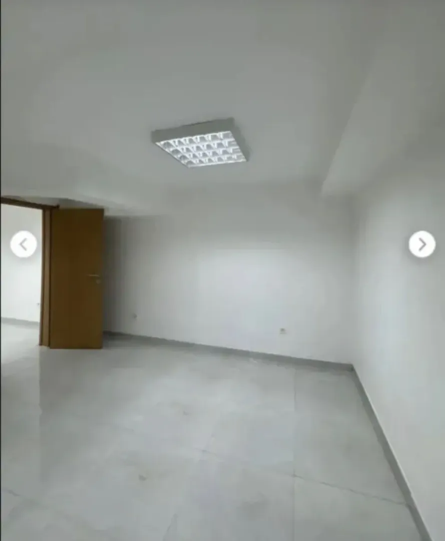 An empty bright room with white walls, tiled floors, and ceiling lighting.