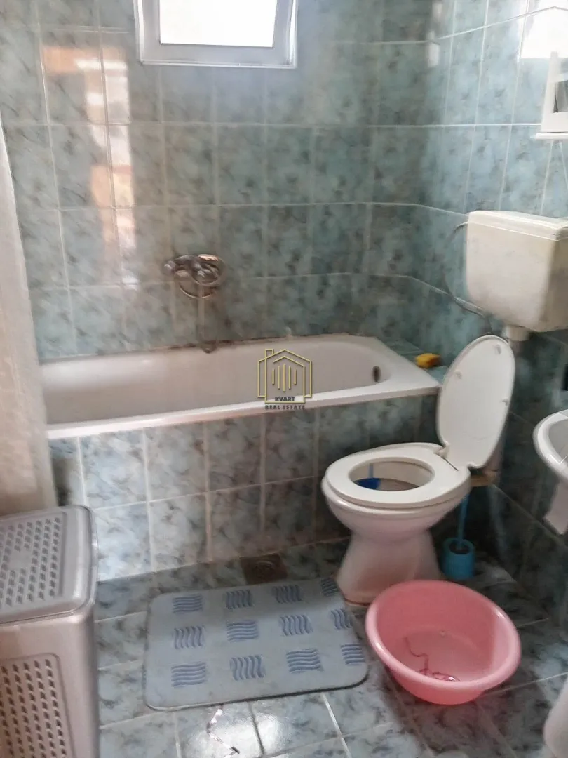 Manje kupatilo obloženo pločicama sa kadom i wc šoljom.