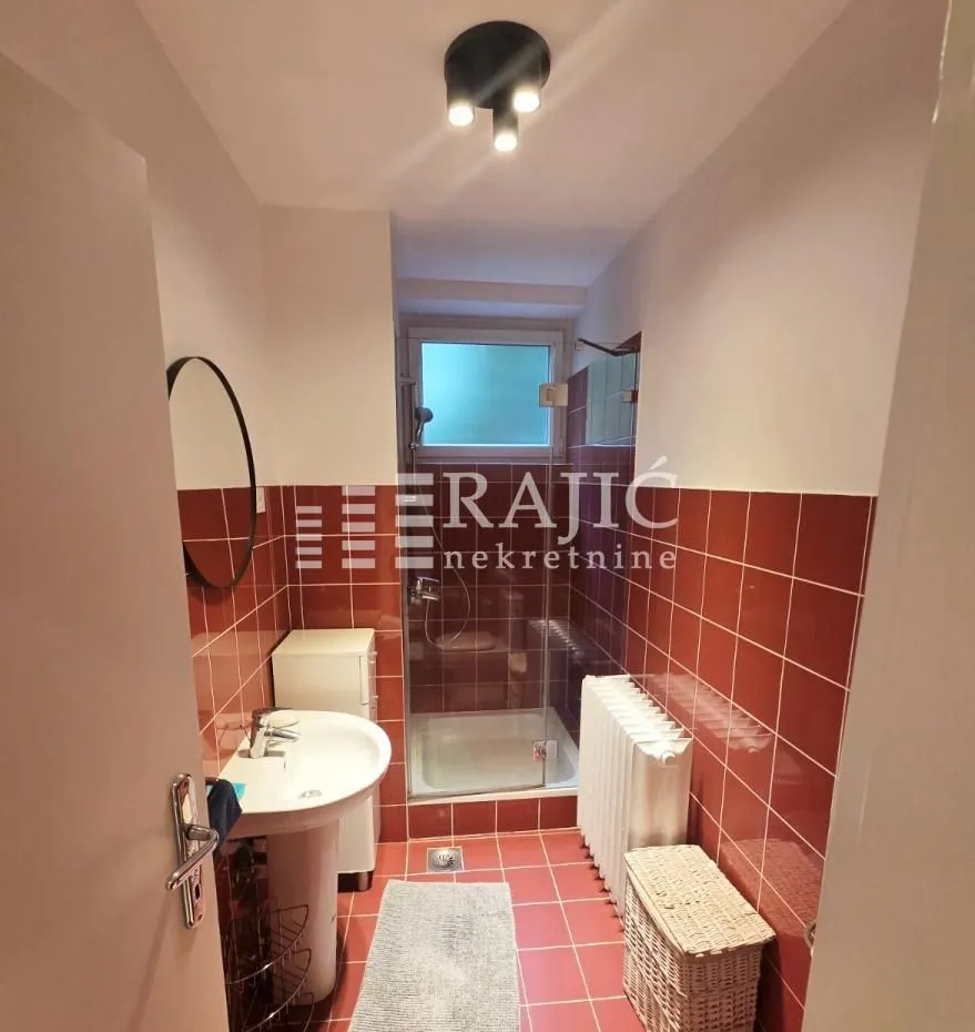 Smaller bathroom lined with red tiles featuring a shower cabin and a washbasin.