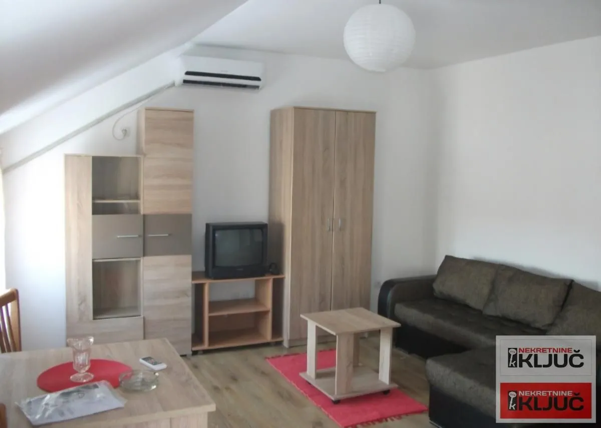 Dnevna soba sa garniturom za sedenje, televizorom i drvenim nameštajem.