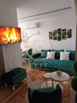 Dnevni boravak sa zelenom garniturom, televizorom i trpezarijskim stolom u pozadini. - image 2
