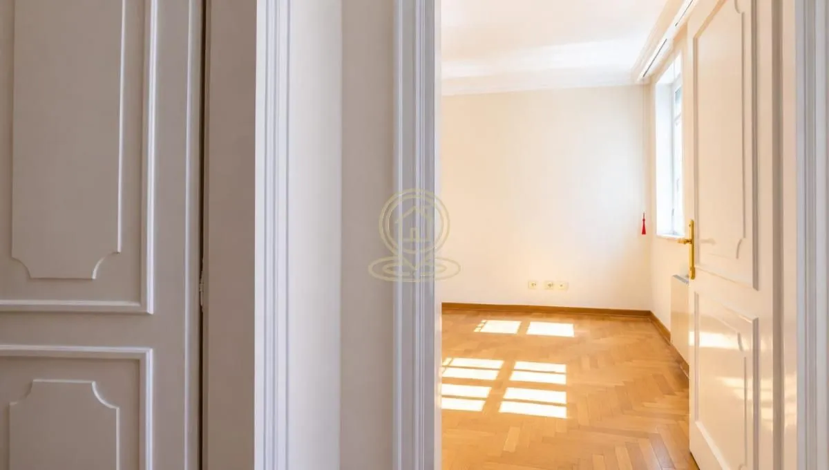 View from the hallway into an empty room with parquet flooring and white doors.
