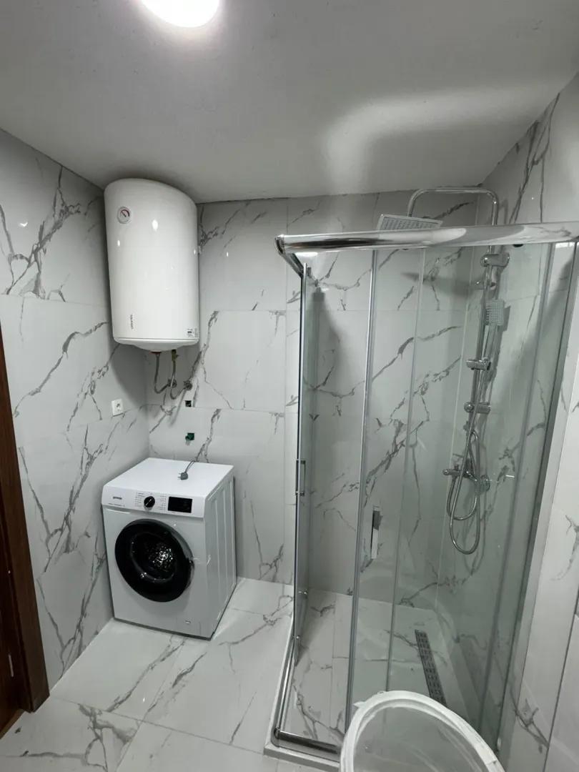 Bathroom with a shower cabin, water heater, and washing machine.