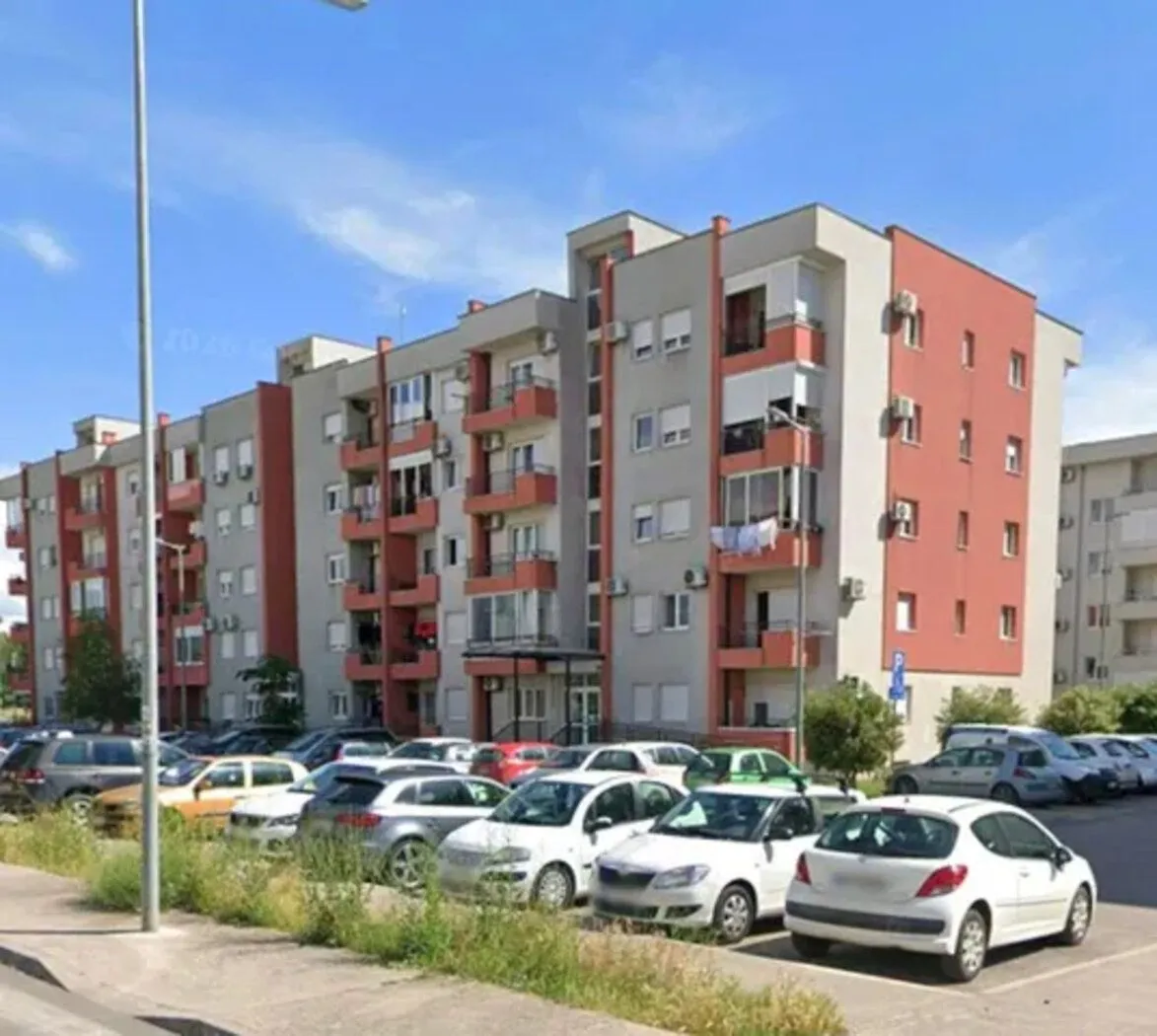 Spoljašnji izgled stambene zgrade sa parkingom ispred.
