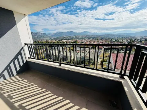 Small balcony with a black railing and a view of the city and mountains. - image 19
