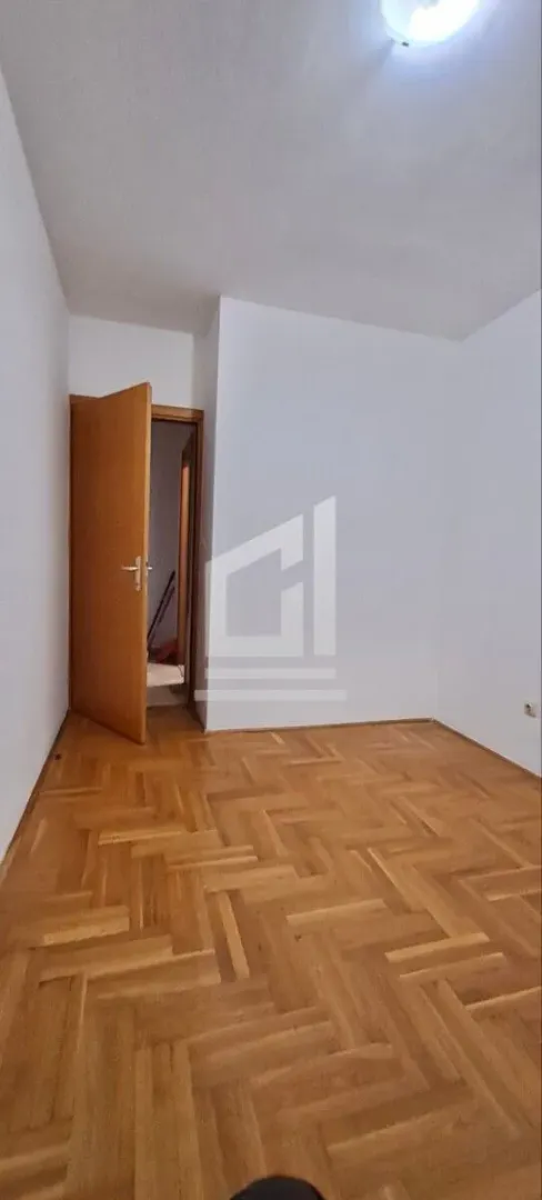Prazna soba sa parketom i otvorenim drvenim vratima.