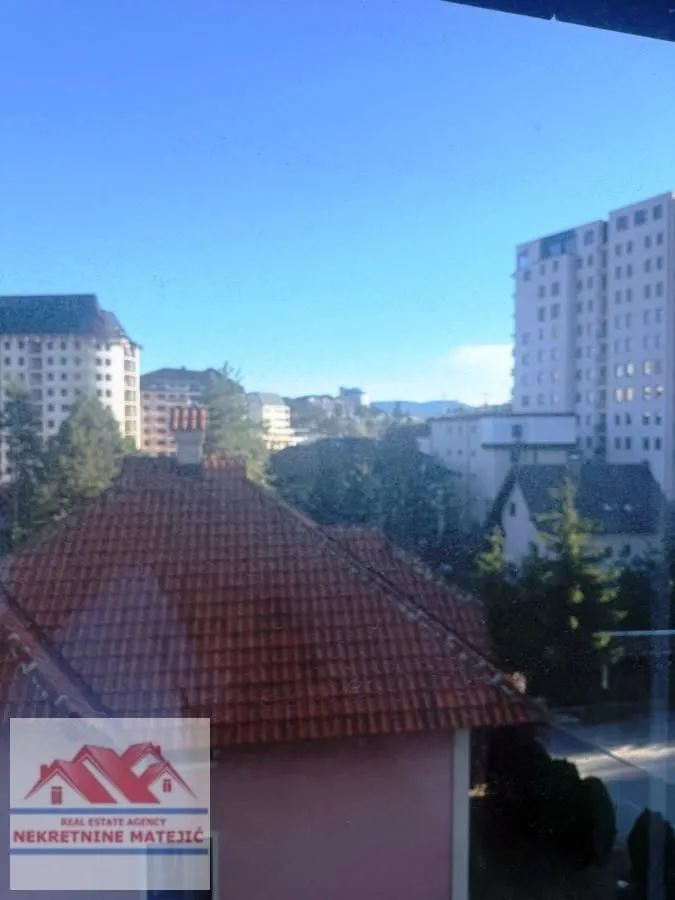 Pogled kroz prozor na okolne zgrade i naselje.