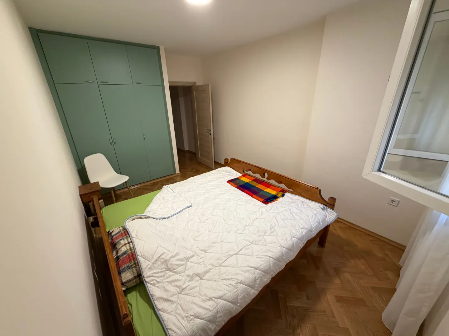 Spavaća soba sa bračnim krevetom, ugradnim ormarom i drvenim podom.