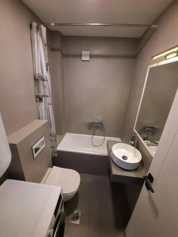 Manje kupatilo sa kadom, umivaonikom i WC šoljom u neutralnim tonovima.