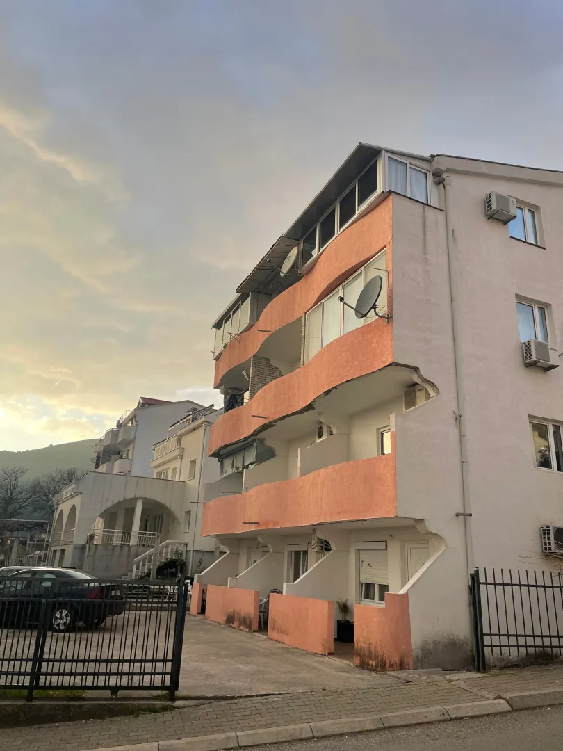 Pogled na spoljašnjost stambene zgrade sa terasama i parkingom u dvorištu.