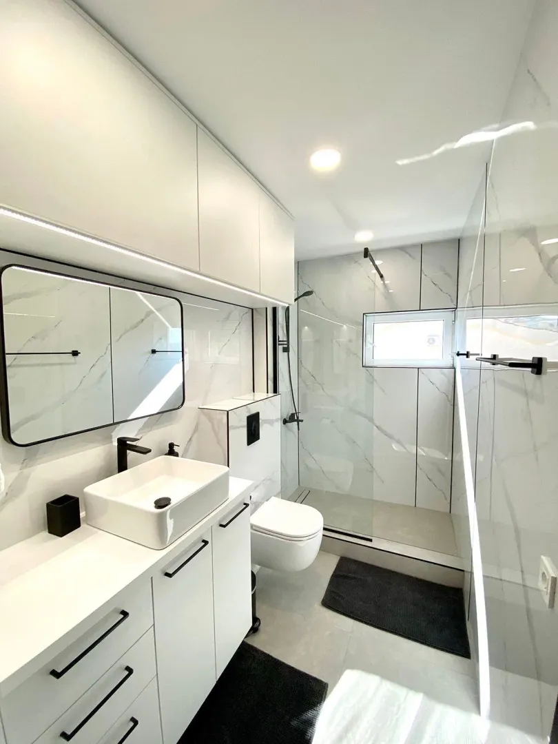 Modernly equipped bathroom with white elements and marble tiles.