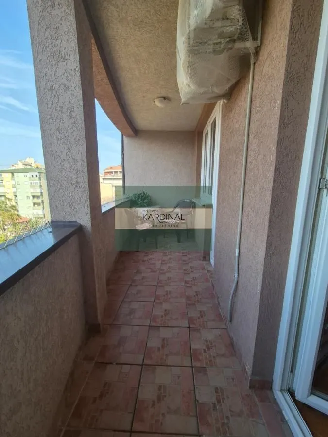 Natkriveni balkon sa popločanim podom i pogledom na okolne zgrade.