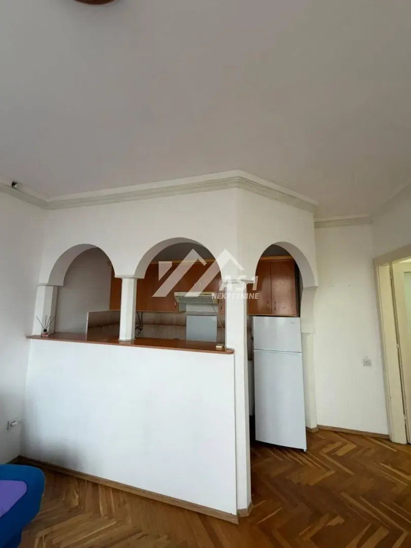Manja kuhinja sa drvenim elementima i pultom sa lukovima.
