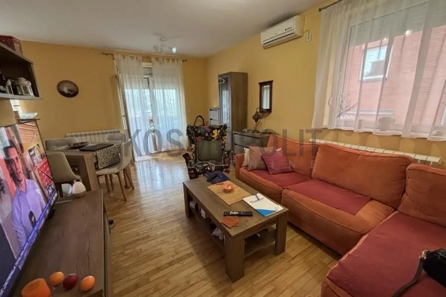 Dnevna soba sa garniturom, drvenim stolom i trpezarijskim delom u pozadini.