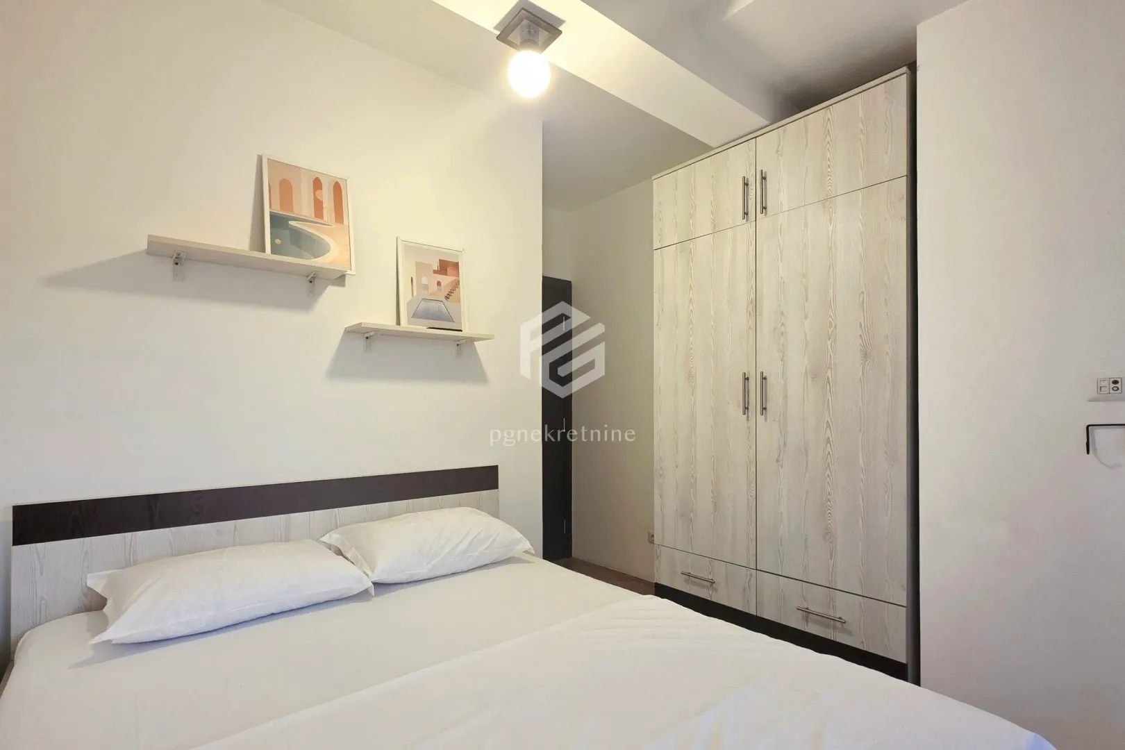 Furnished bedroom with a double bed, wardrobe, and wall shelves.