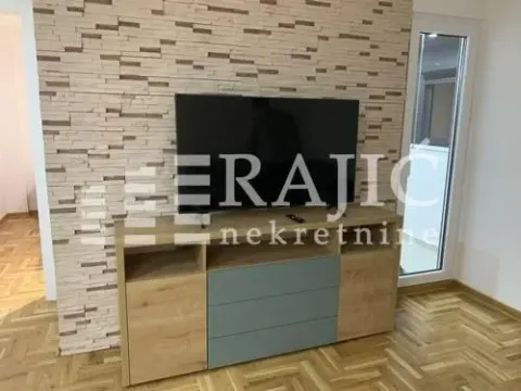 Living room with a TV and a chest of drawers in front of a decorative stone wall. - image 3
