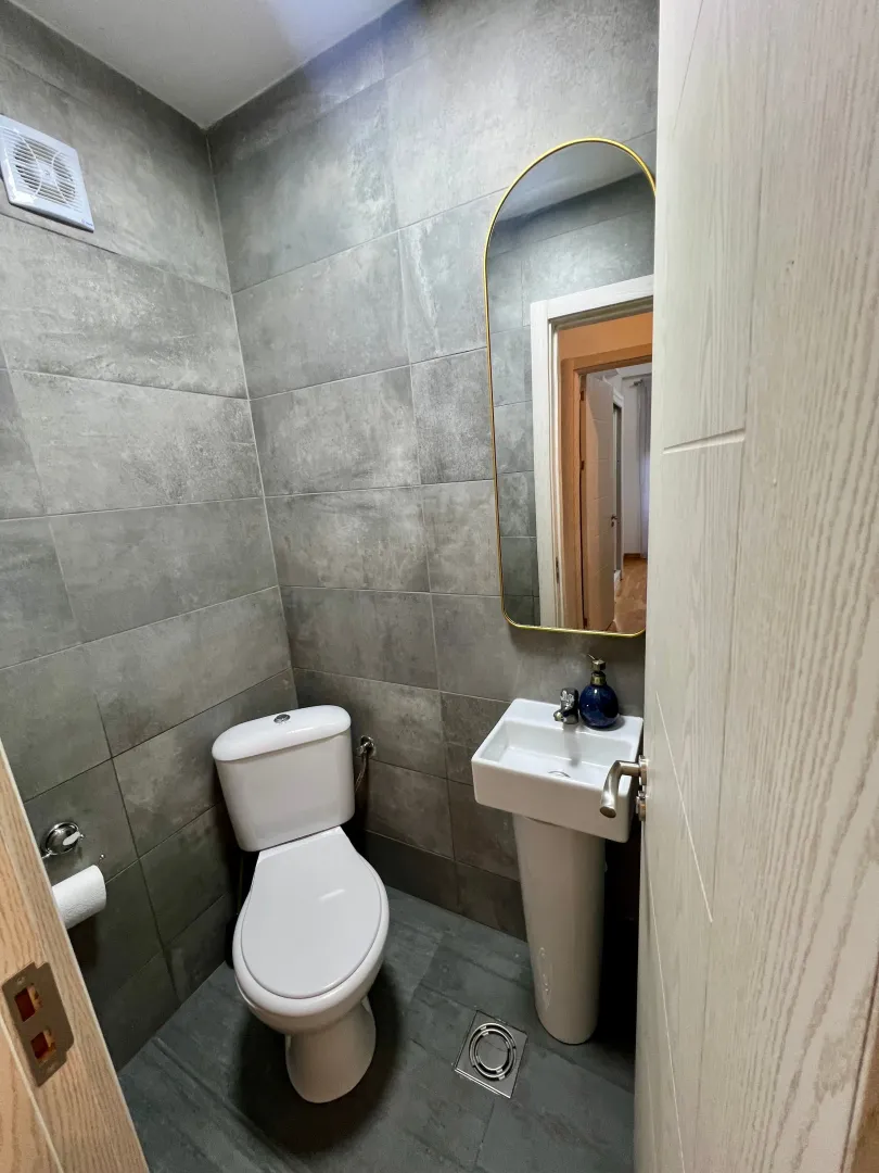 Small bathroom with grey tiles, a sink, and a toilet.