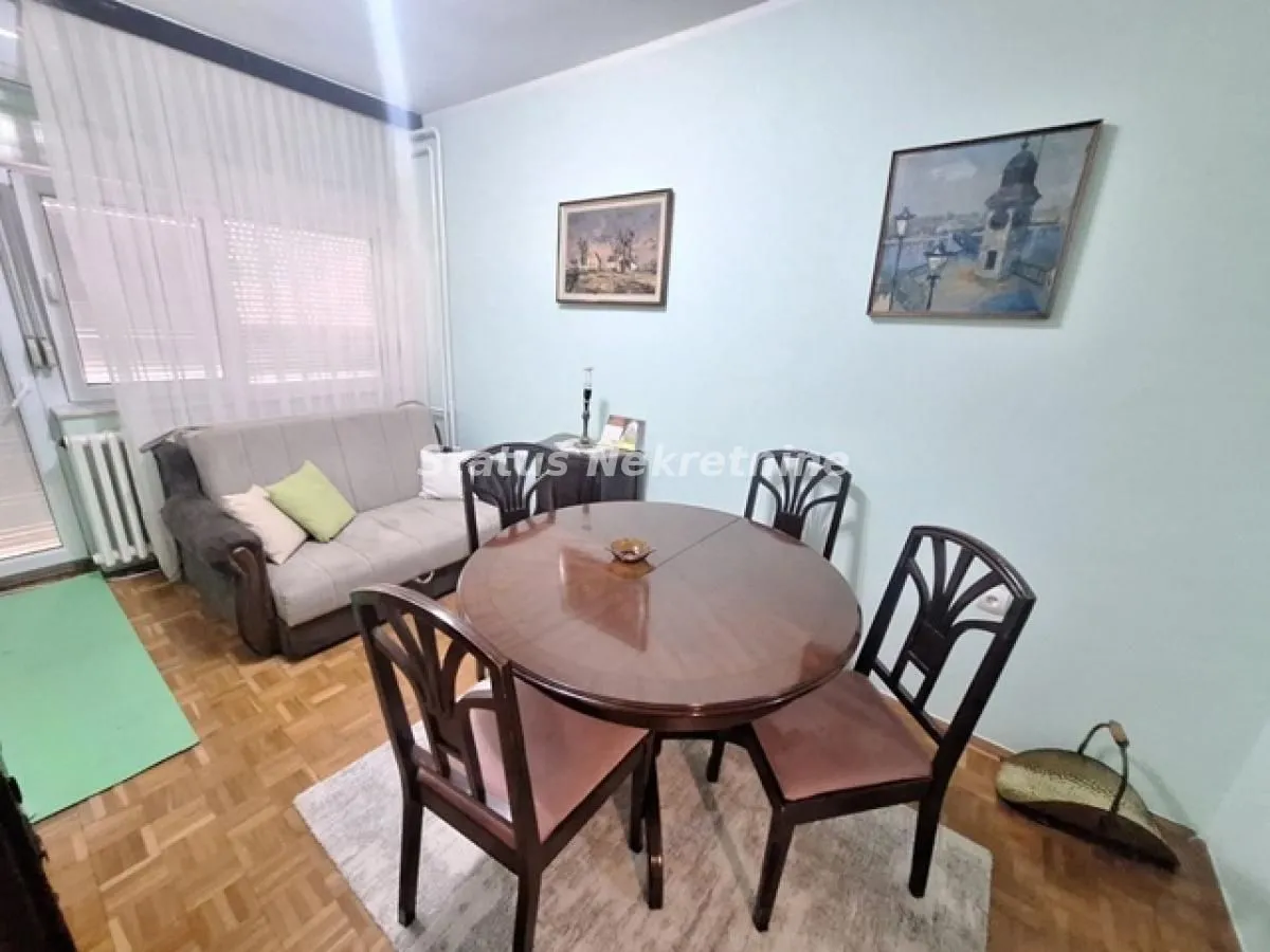 Dnevna soba sa garniturom za sedenje, trpezarijskim stolom i slikama na zidu.
