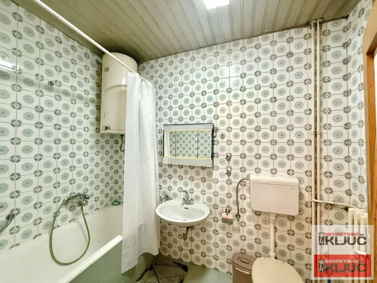 Starije opremljeno kupatilo sa kadom, umivaonikom, WC šoljom i bojlerom.