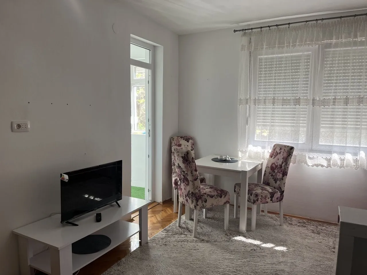 A bright living room featuring a small dining table and a television.