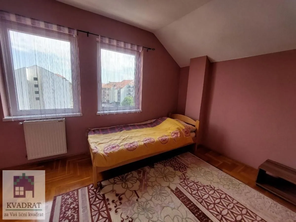Smaller bedroom with a bed, parquet flooring, and two windows.