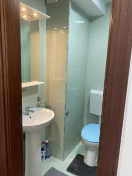 A bathroom with light green tiles, a pedestal sink, and a toilet viewed through a doorway. - image 7