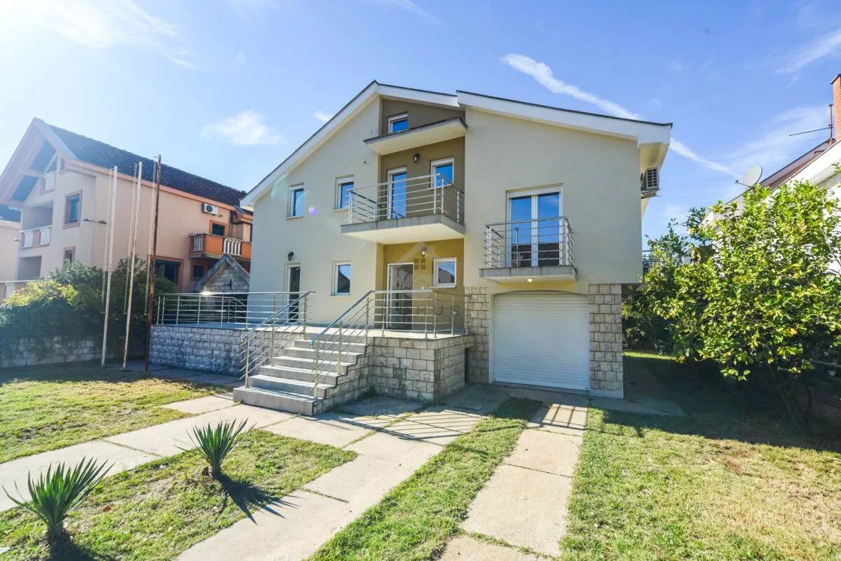 Front view of a multi-story house with a landscaped yard, balconies, and a garage.