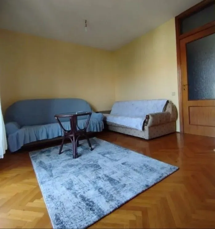 A simple living room with two sofas, a small table, and a rug on parquet flooring.