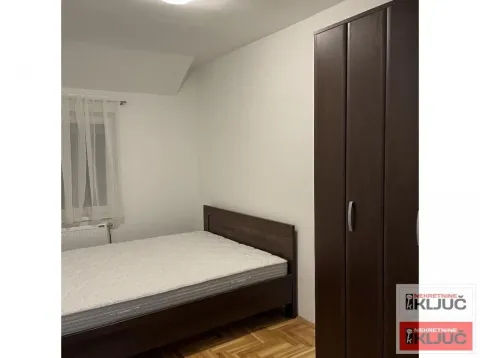 Manja spavaća soba sa krevetom i tamnim drvenim ormarom. - image 7
