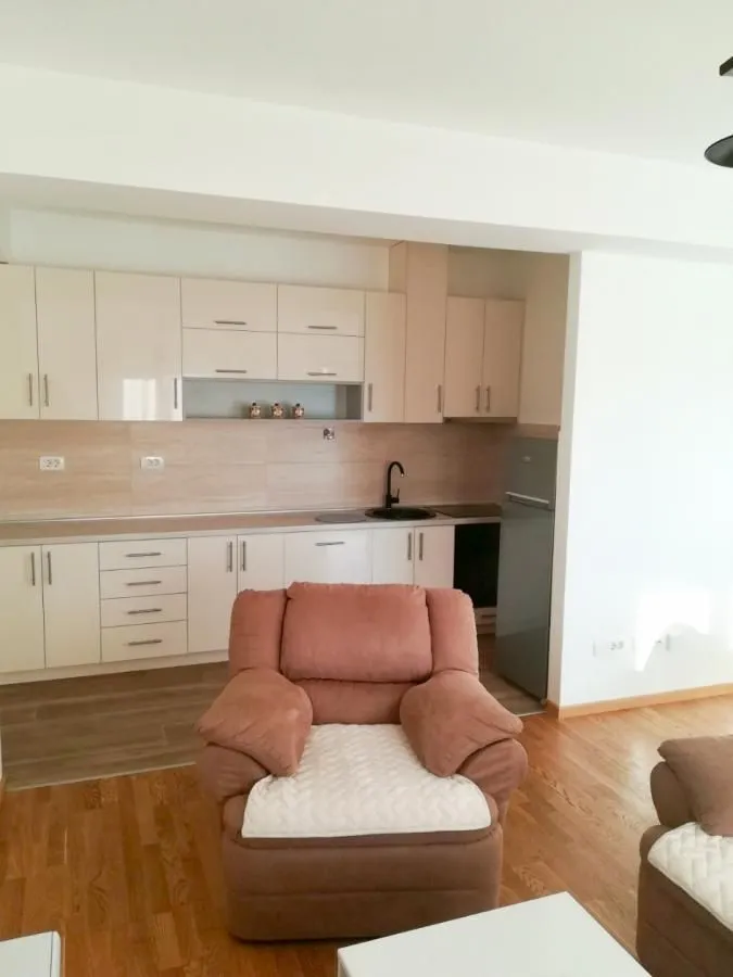 Living room with a sofa set and a fitted kitchen in the background.