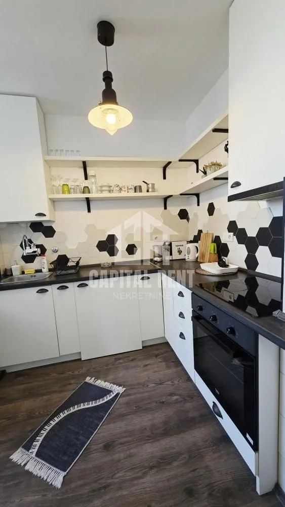 Modern white kitchen with black elements and hexagonal wall tiles.
