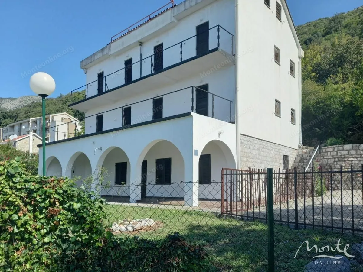 Exterior view of a white multi-story house with terraces and a yard.