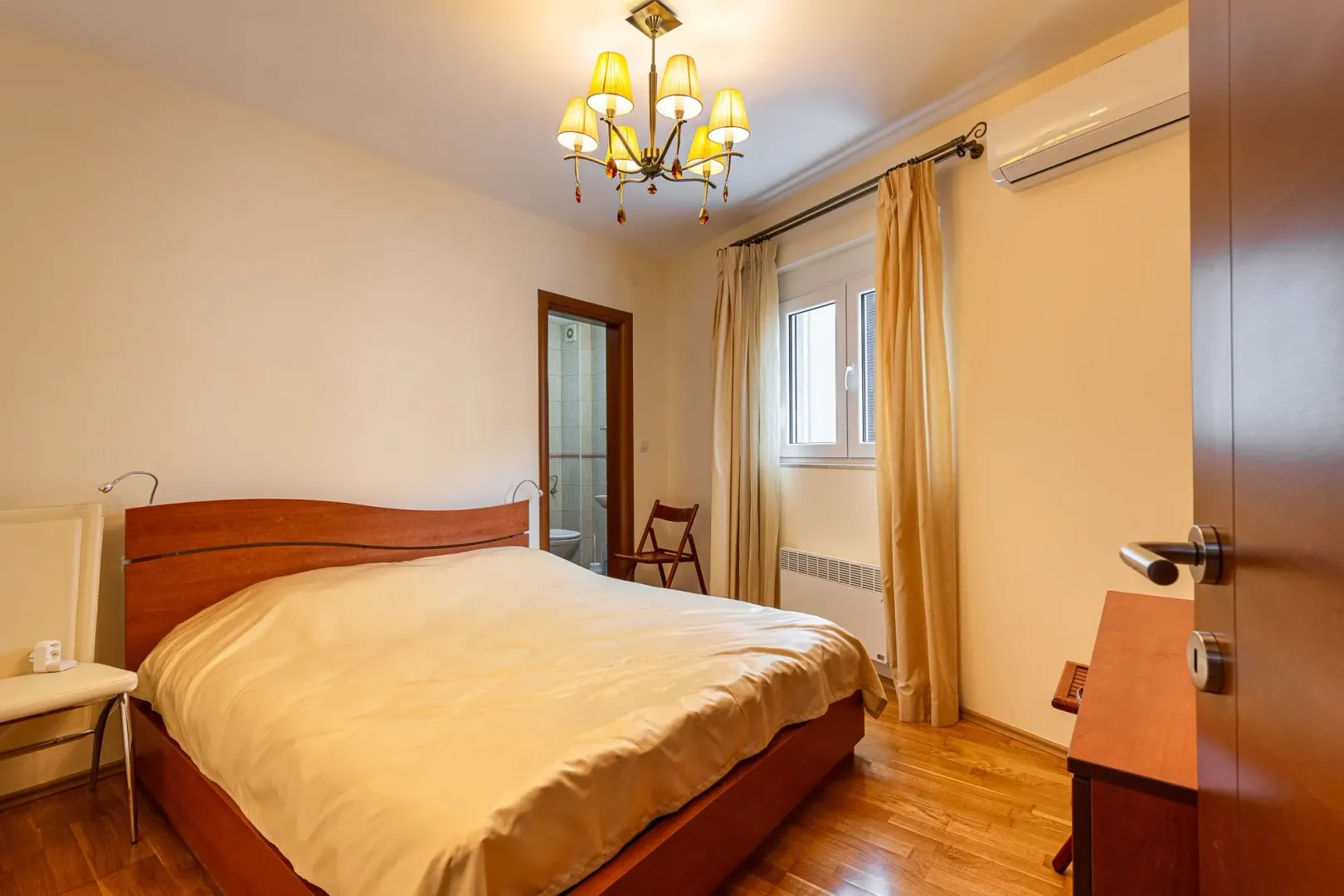 Furnished bedroom with a double bed, a window, and a view into the bathroom.