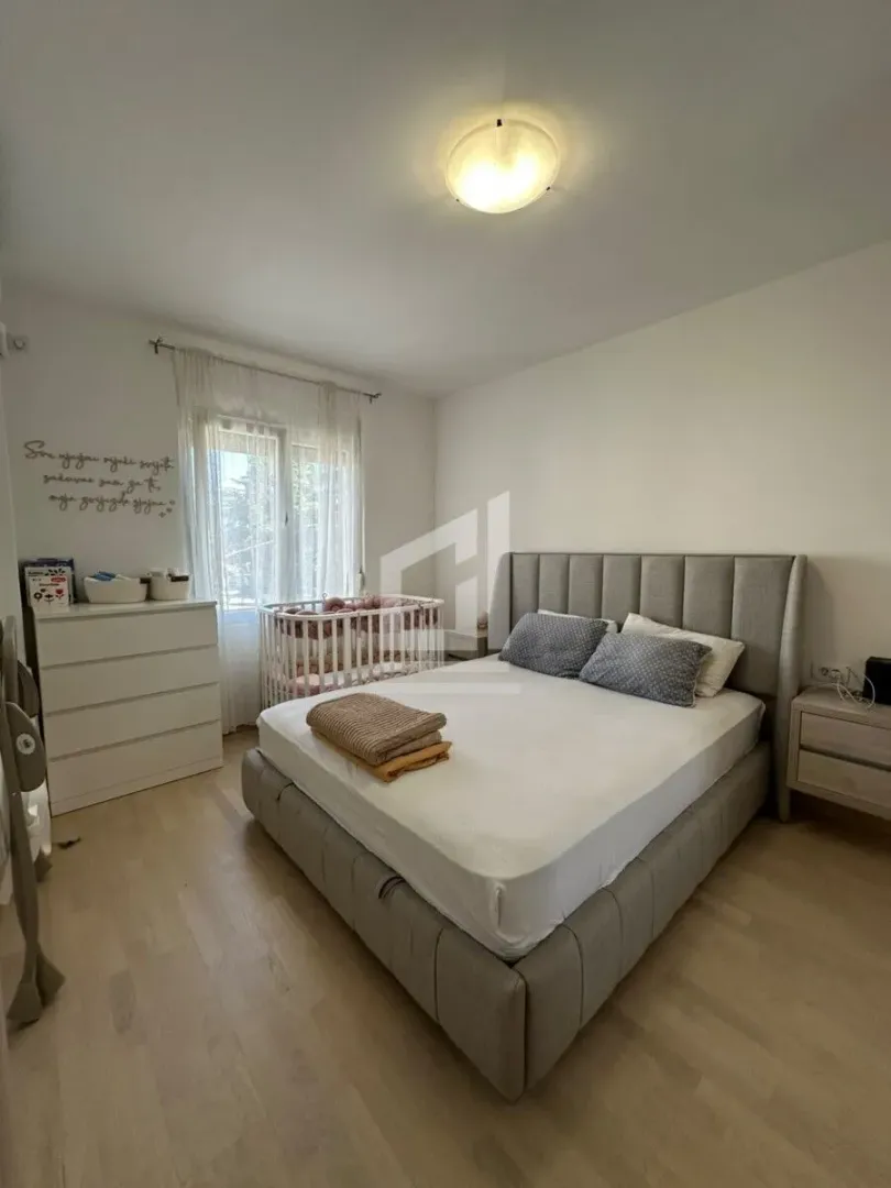 Namještena spavaća soba sa bračnim krevetom, krevetcem i prozorom.