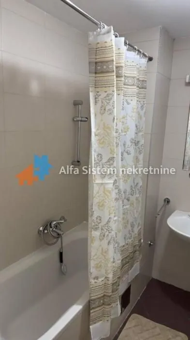 Kupatilo opremljeno kadom, umivaonikom i zavesom za tuširanje.