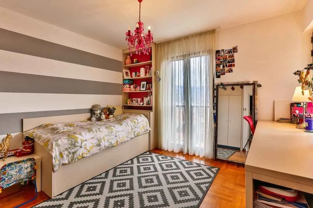 Bright children's bedroom with a bed, study desk, and striped wall.
