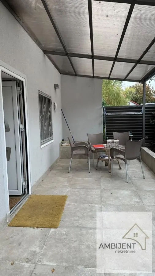 Natkrivena terasa sa stolom i stolicama ispred ulaza u kuću.