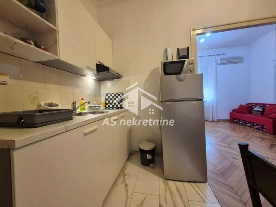 Compact kitchen with white cabinetry and a refrigerator, with a view into the adjacent room.